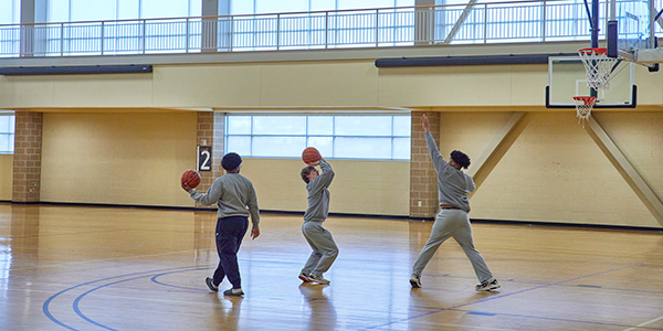 Three students shooting basketballs together.